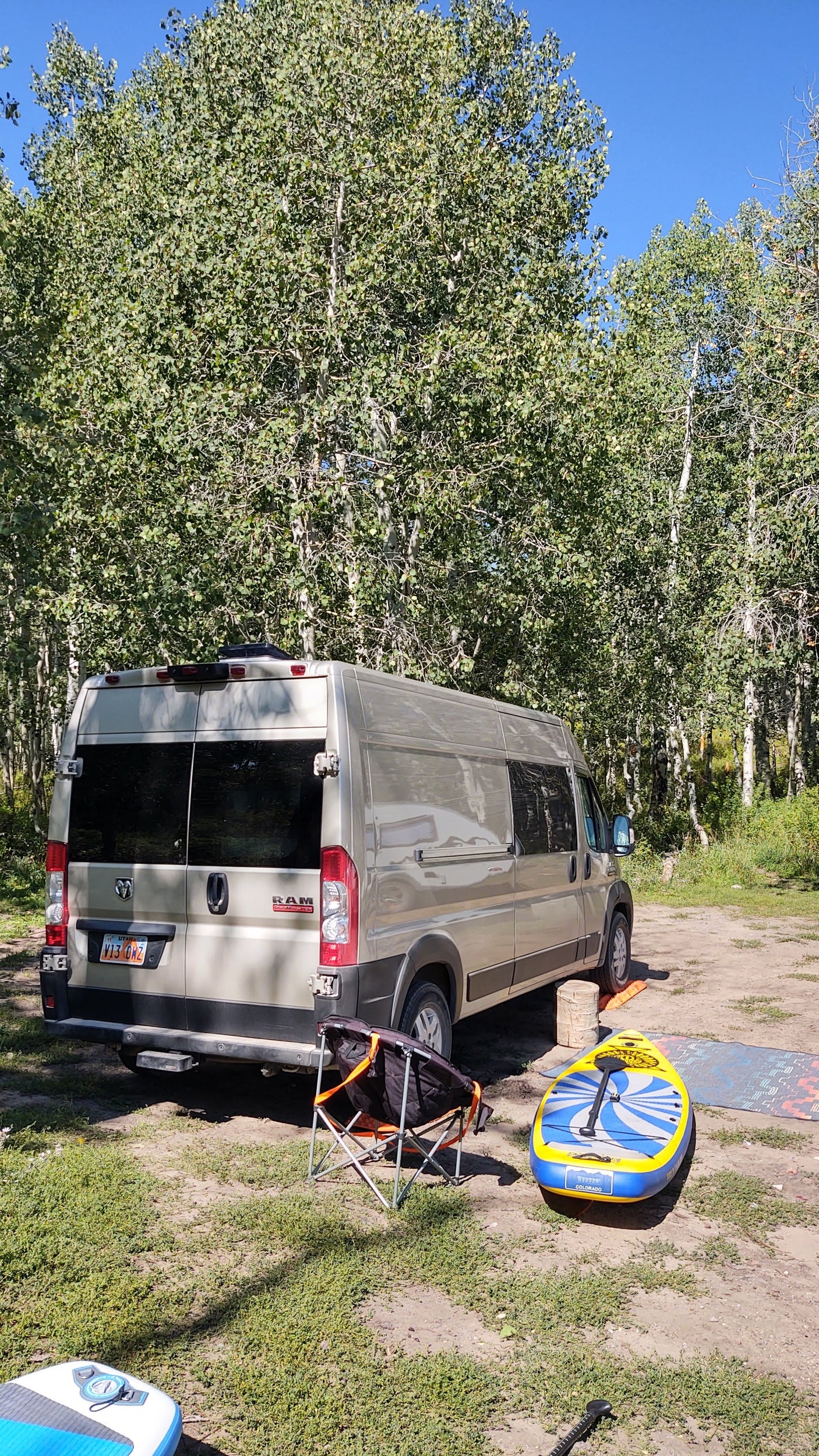 RV rental van parked at a peaceful campsite among Aspen trees, with paddleboards and camping gear ready for adventure.