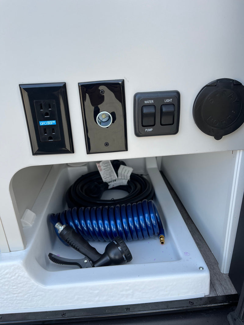 RV rental outdoor utility panel: GFCI outlet, 12V socket, water/light switches, spray hose, and sink basin. — photo 12