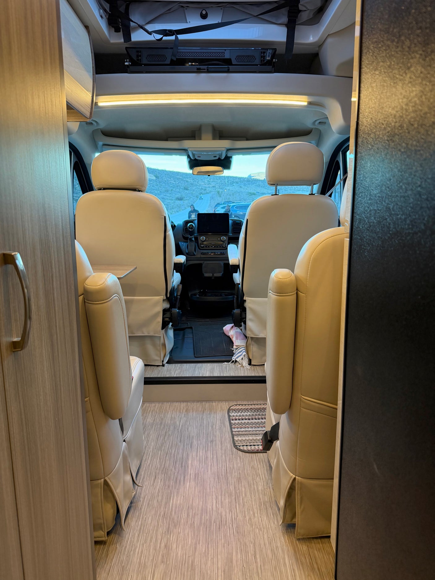 RV rental interior: Looking forward at the front cabin with plush beige seats, dashboard, and a desert road view.