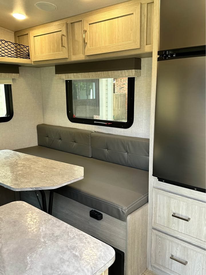 Explore this rv rental's modern interior: a bright dinette with light wood cabinets, grey tufted seating, and a window view. — photo 5