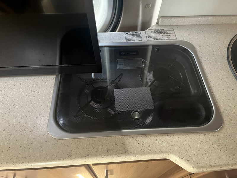 RV rental kitchen: Dometic two-burner cooktop with cover and warning labels on a light-colored counter. — photo 19