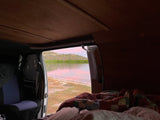Peaceful pink-hued waters seen from an RV rental's cozy interior, featuring a wooded ceiling and warm bedding by the shore.