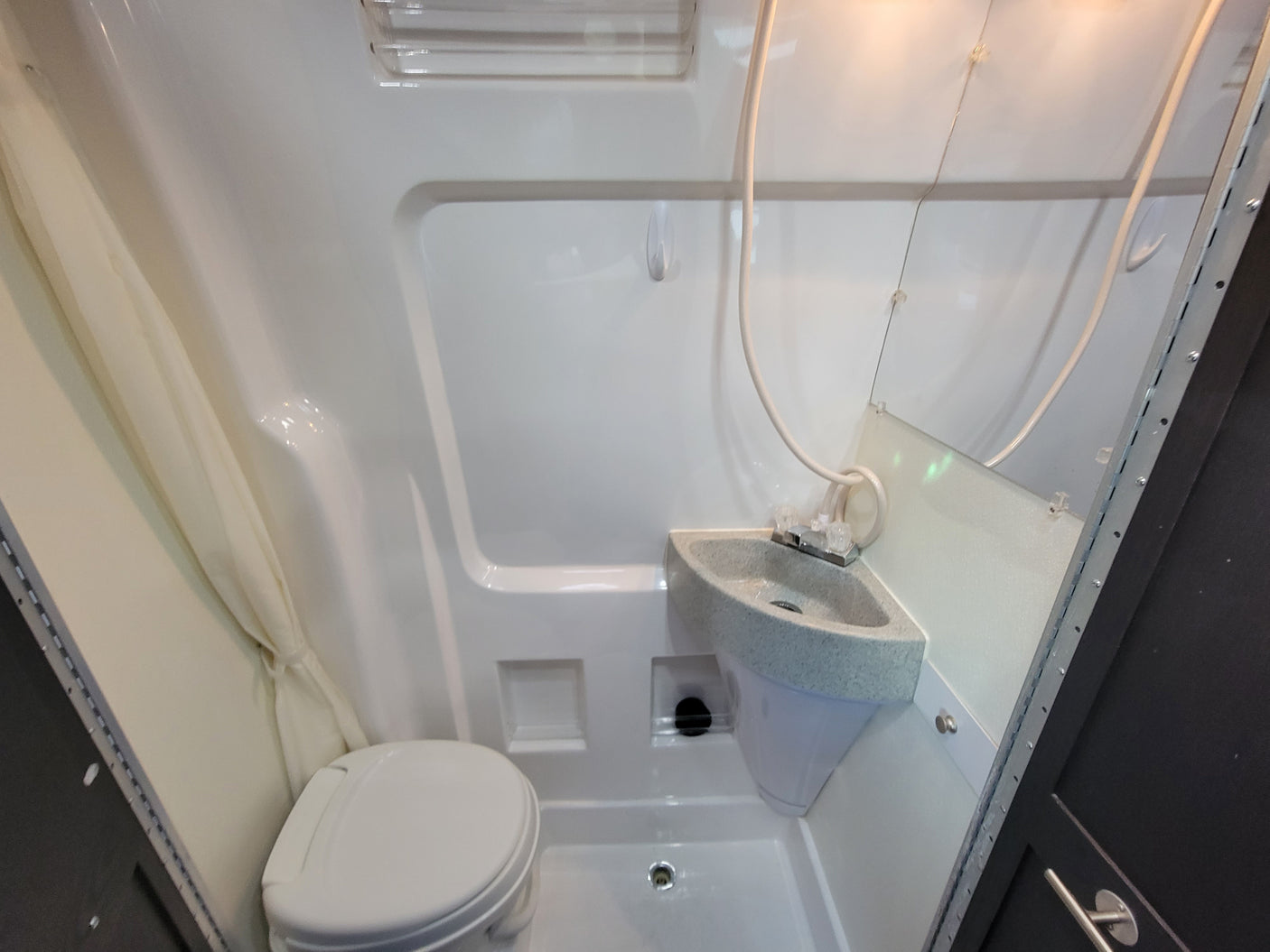 Compact RV rental bathroom with integrated toilet, corner sink, and shower for efficient space use on the go.