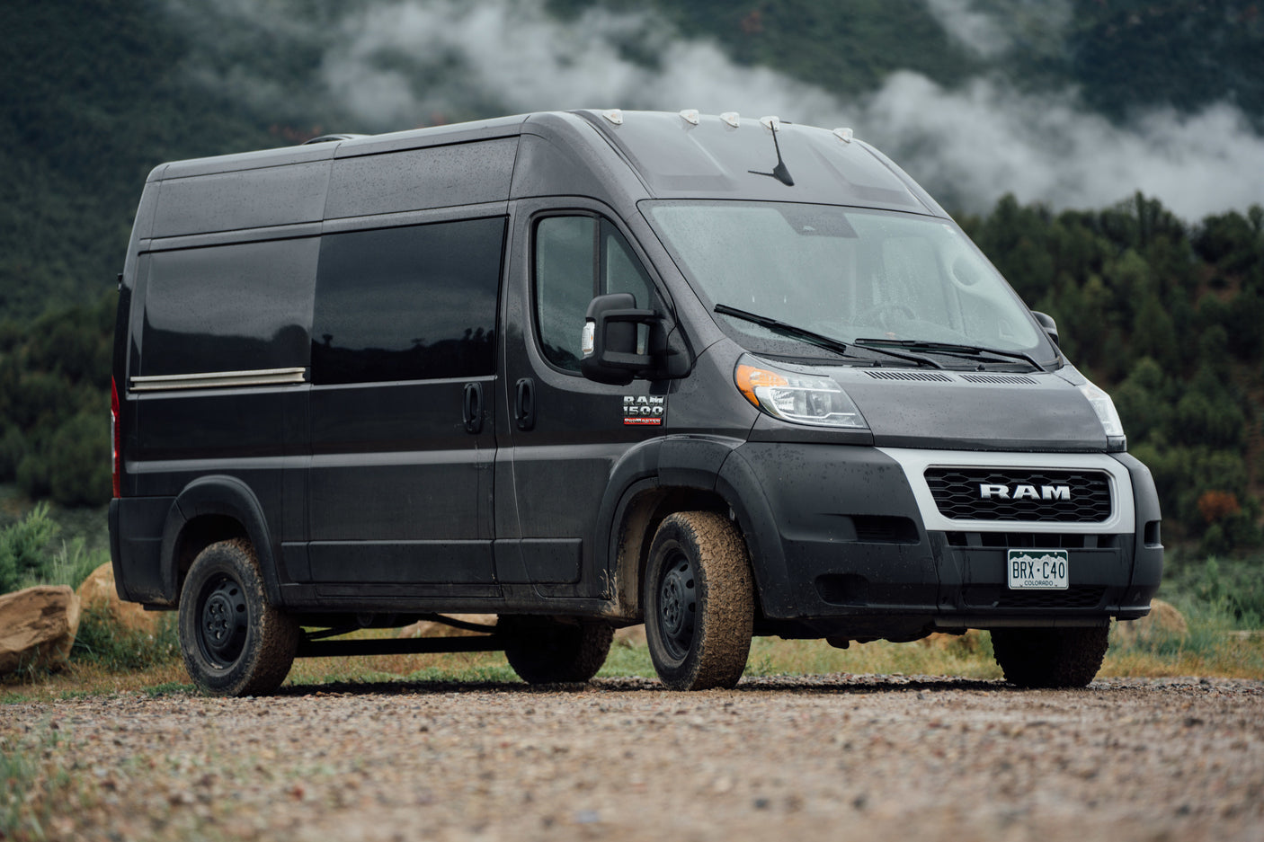 Explore mountains with this muddy dark grey Ram Promaster rv rental camper van, ready for adventure.