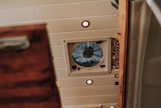Ceiling of an RV rental showing a powered vent fan, recessed LED lights, and white wood paneling, offering comfort.
