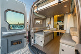 Experience comfort in this RV rental! Open doors reveal a cozy camper van interior with dining area and bed, perfect for mobile adventures.
