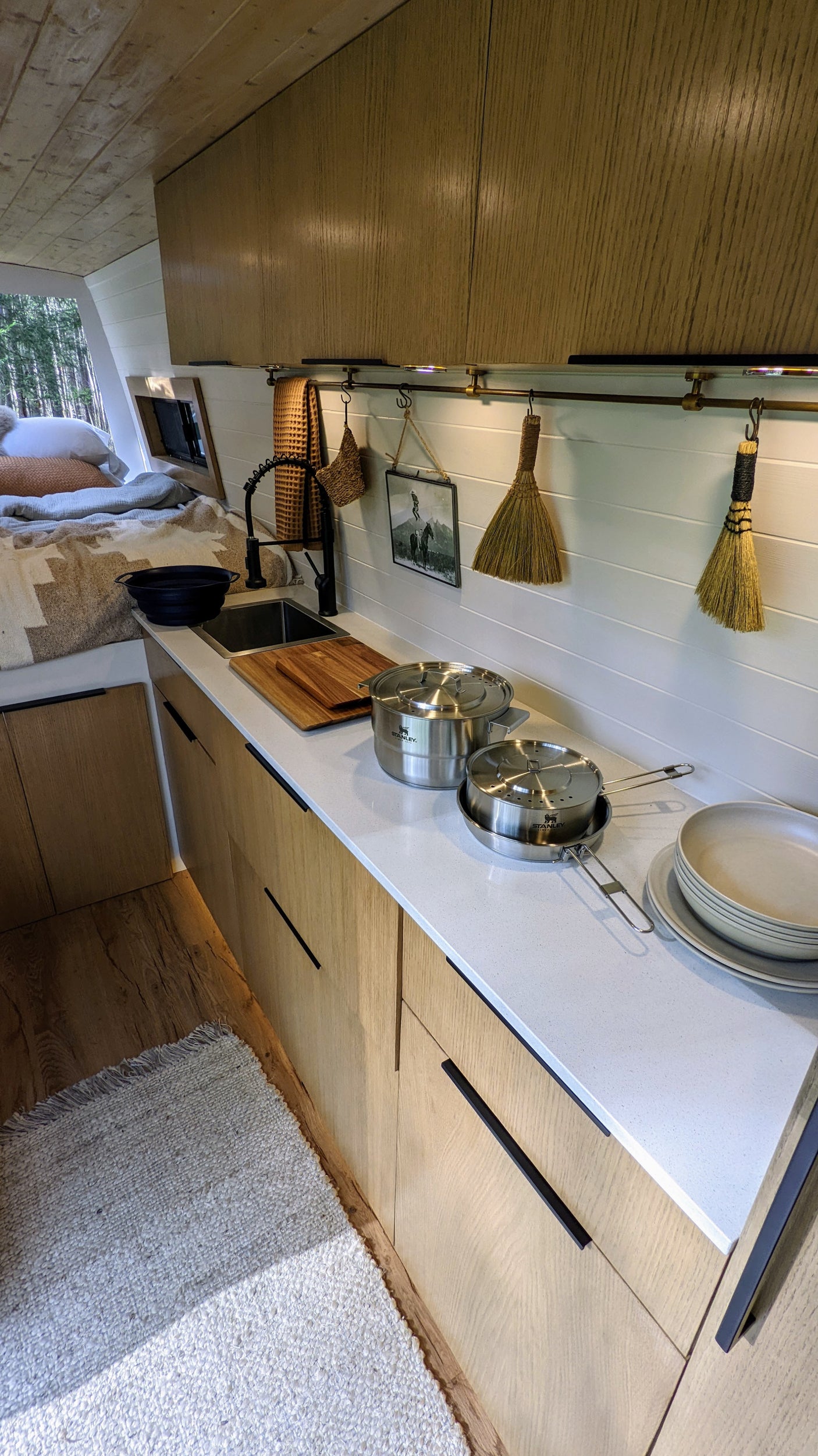 Step into this cozy RV rental interior, featuring a modern kitchen, comfortable bed, and scenic forest views.