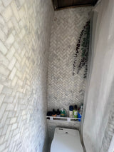 An RV rental's compact bathroom: white herringbone tile walls, toilet, shelf of toiletries, and a shower curtain.