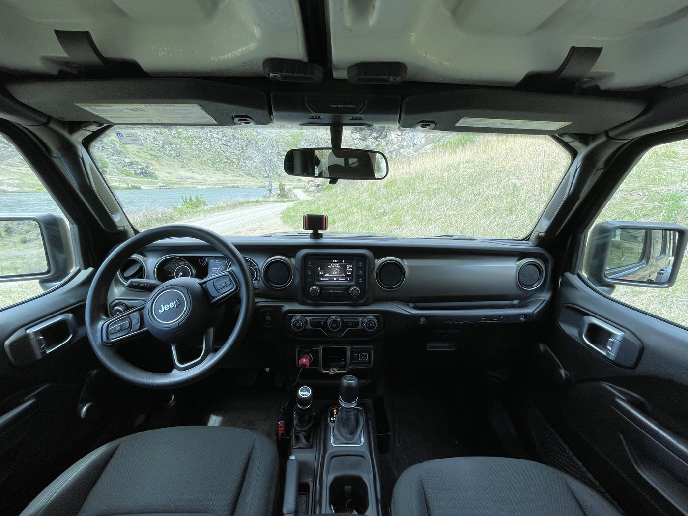 Jeep Wrangler interior, steering wheel visible. Scenic view of a lake & dirt road. Perfect for off-road travel or an RV rental adventure. — photo 14
