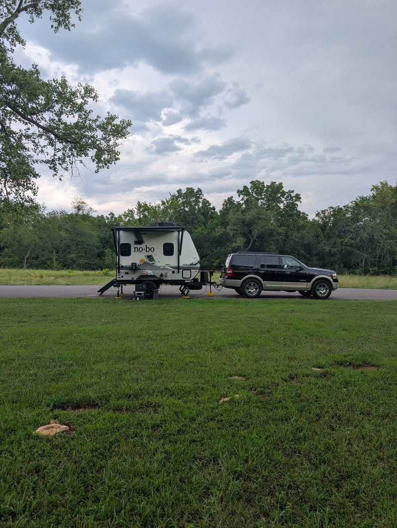 No Boundaries RV rental trailer hitched to a black SUV, set up for camping on a grassy site under cloudy skies. — photo 18