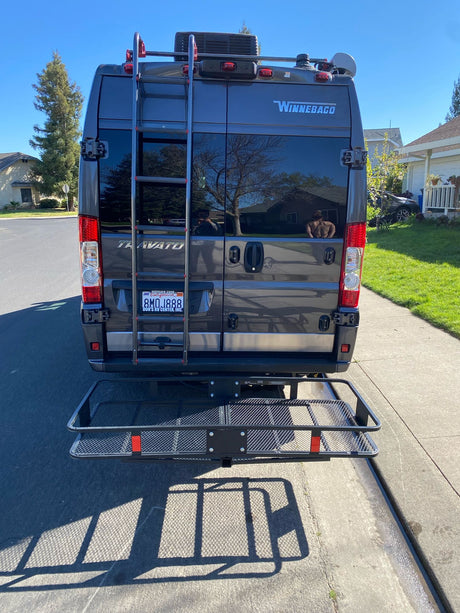 Grey Winnebago Travato RV rental from rear, featuring a ladder & cargo carrier. Parked on a sunny street, ready for adventure.