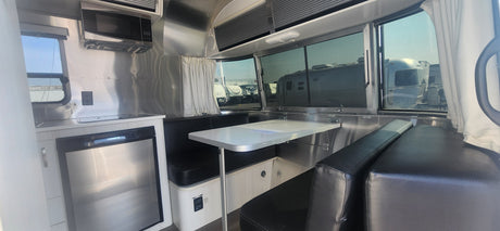 Step inside this Airstream RV rental: a compact kitchen with a Dometic fridge and a cozy dinette with black benches.