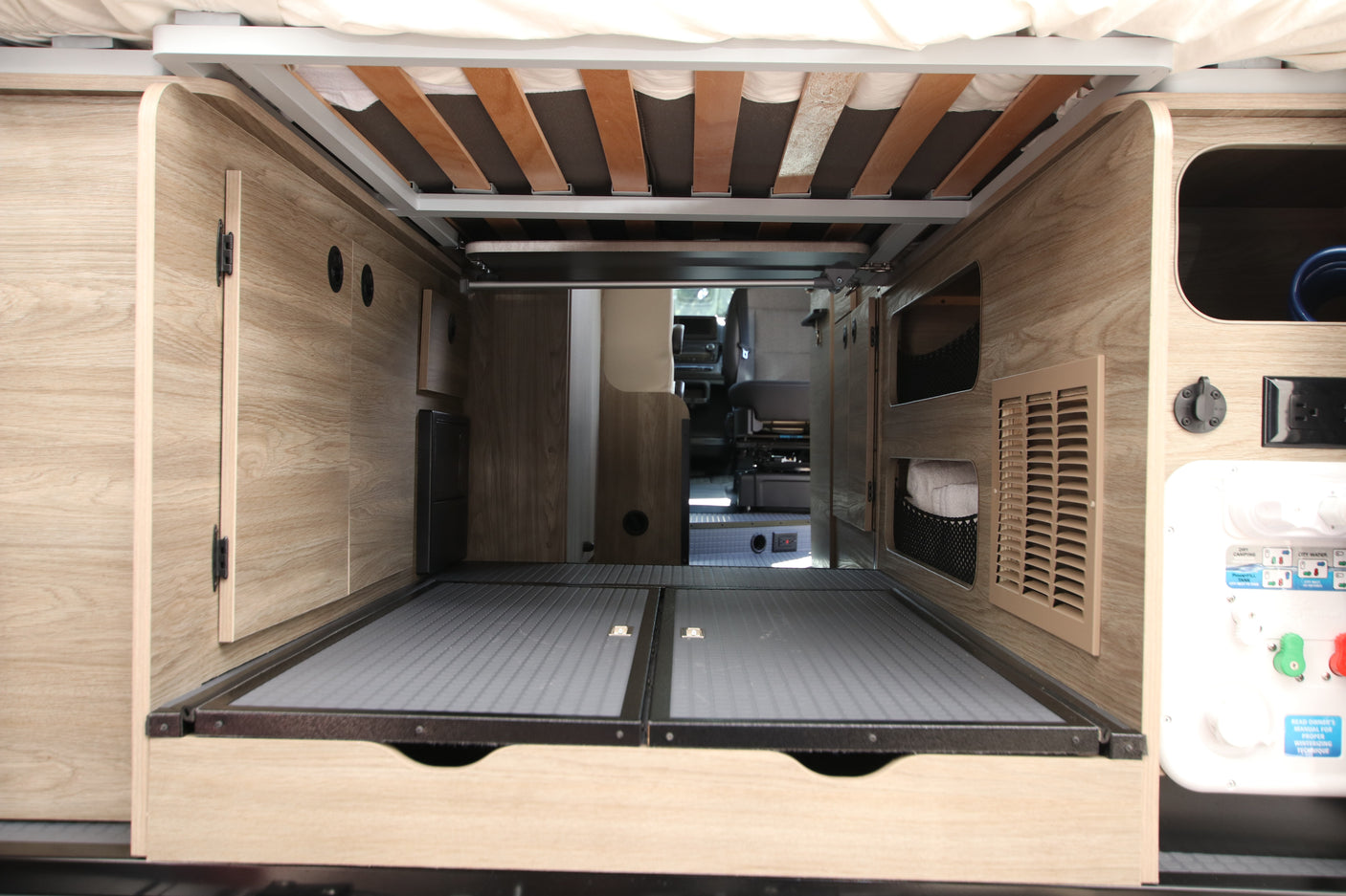 This RV rental features a large under-bed storage area, revealing bed slats, interior paneling, and a view into the main cabin.