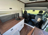 Explore this clean RV rental interior featuring a full kitchen with sink, dark wood counters, white cabinets, and front seats.