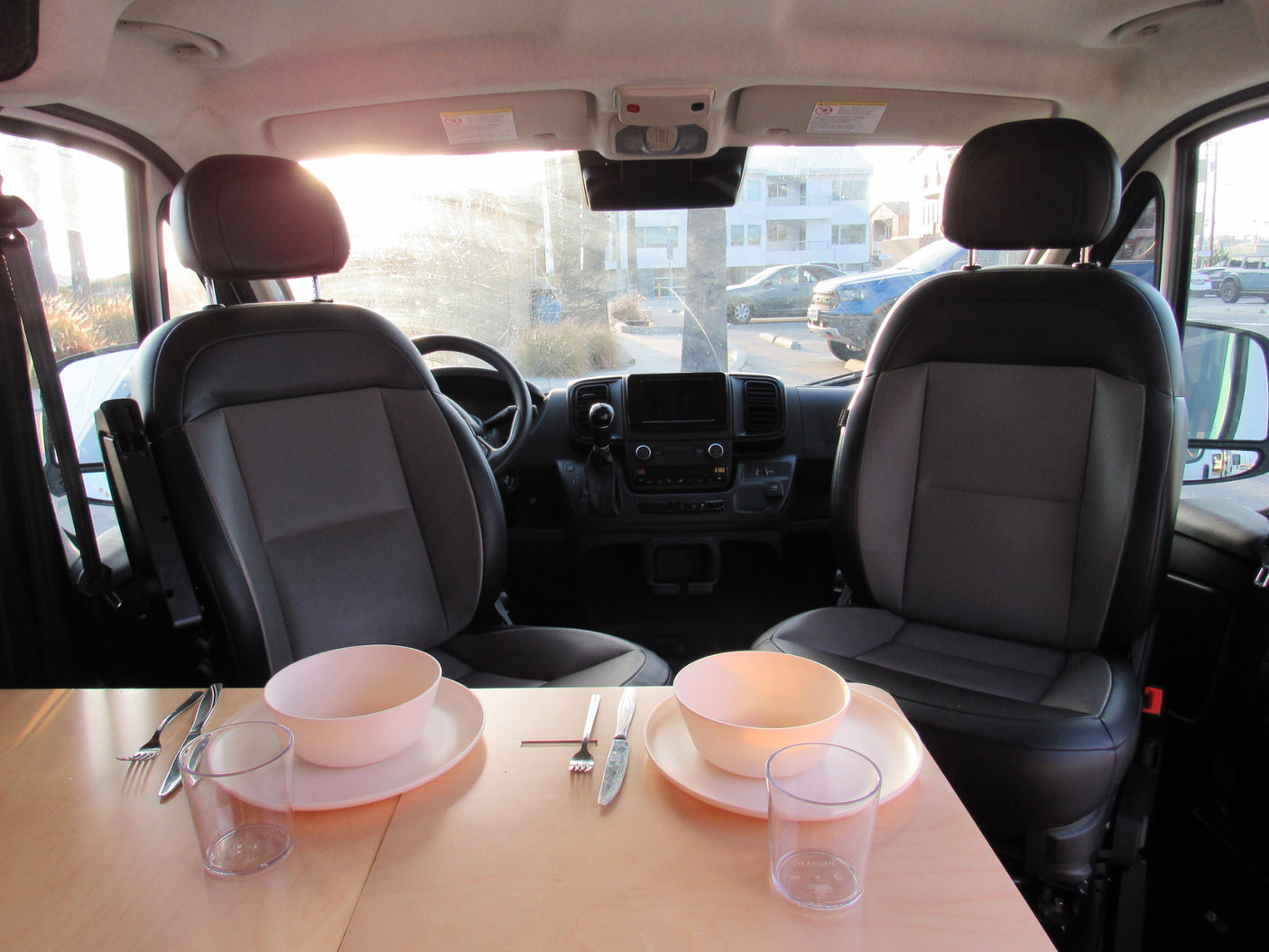 Cozy interior of an RV rental camper van with front seats and a dining table set for two. Bright view out the windshield.