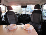 Cozy interior of an RV rental camper van with front seats and a dining table set for two. Bright view out the windshield.