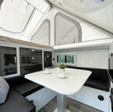 Cozy RV rental interior: pop-top roof, dinette with light table, black seating, and modern storage cabinets.