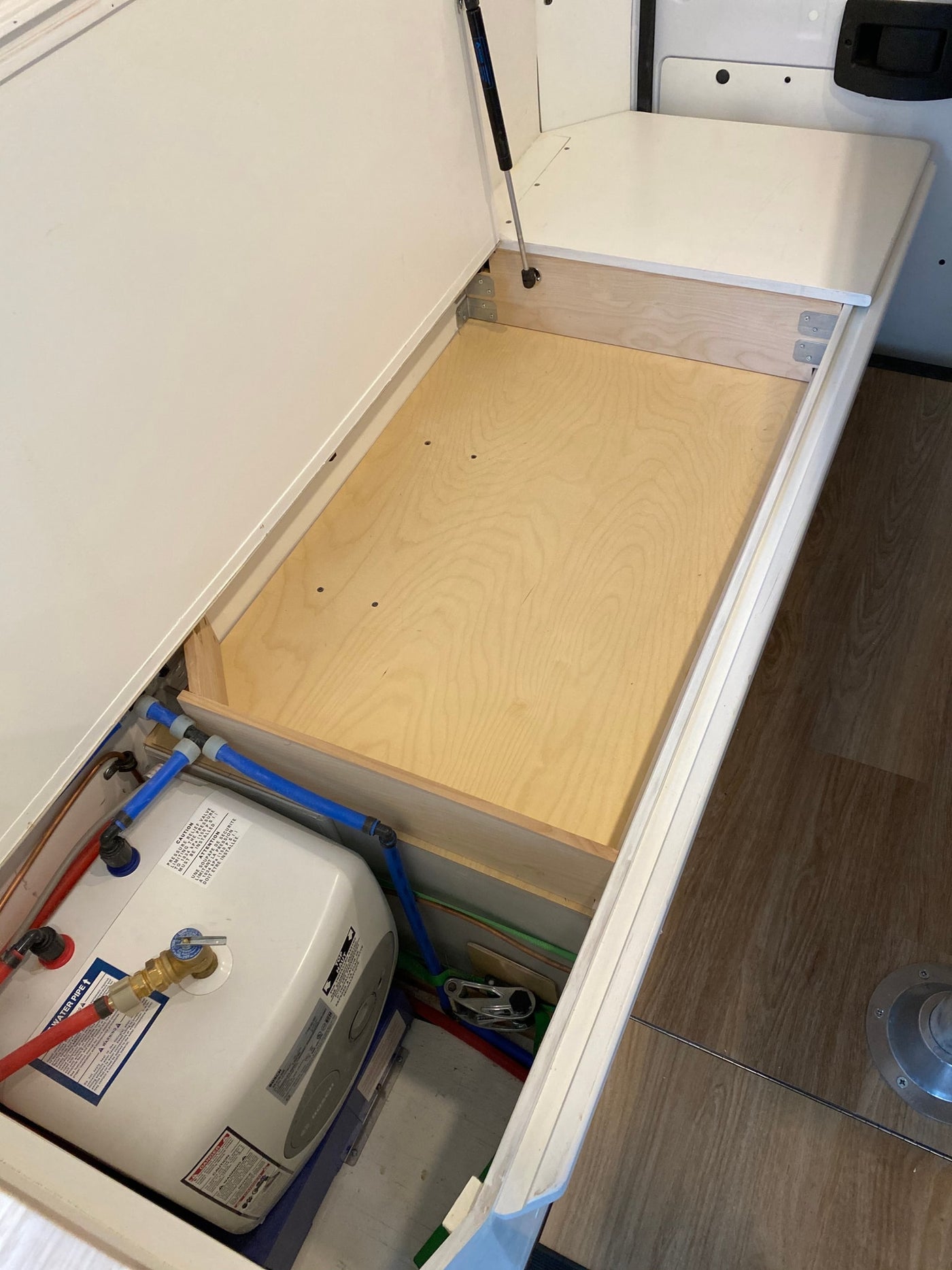 RV rental storage lifts to show a compact water heater and blue plumbing lines. Efficient use of space for travel. — photo 15