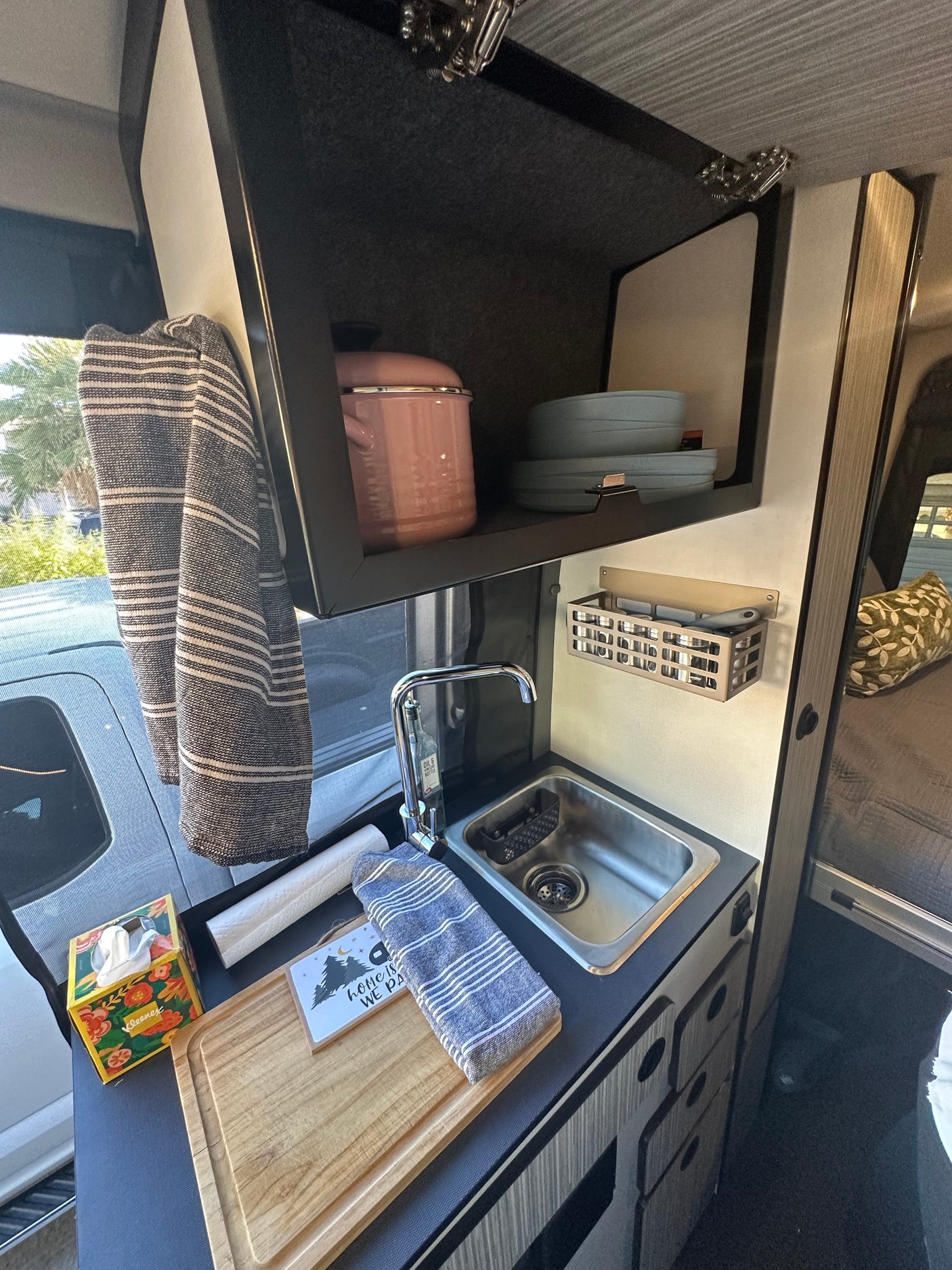 This rv rental showcases a functional kitchen with a sink, overhead cabinet for dishes/pot, and countertop prep space.