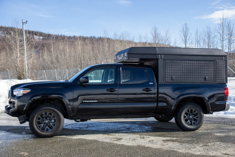 This black Toyota Tacoma pickup truck, equipped with a heavy-duty truck bed camper, is ideal for an RV rental adventure.