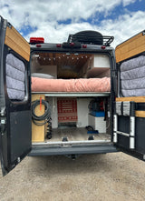 This converted camper van with an open rear reveals a cozy bed, storage, and custom interior, perfect for an RV rental adventure.