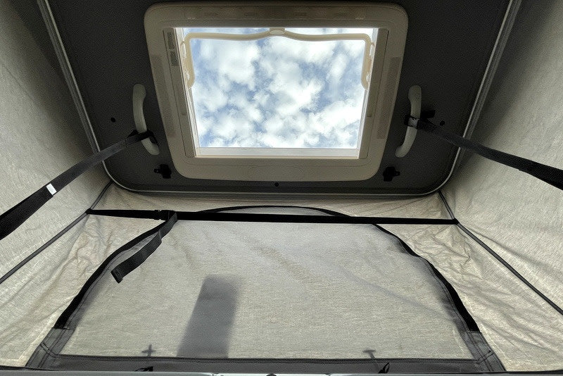 RV rental interior with an open pop-top skylight, revealing cloudy skies above the fabric walls.