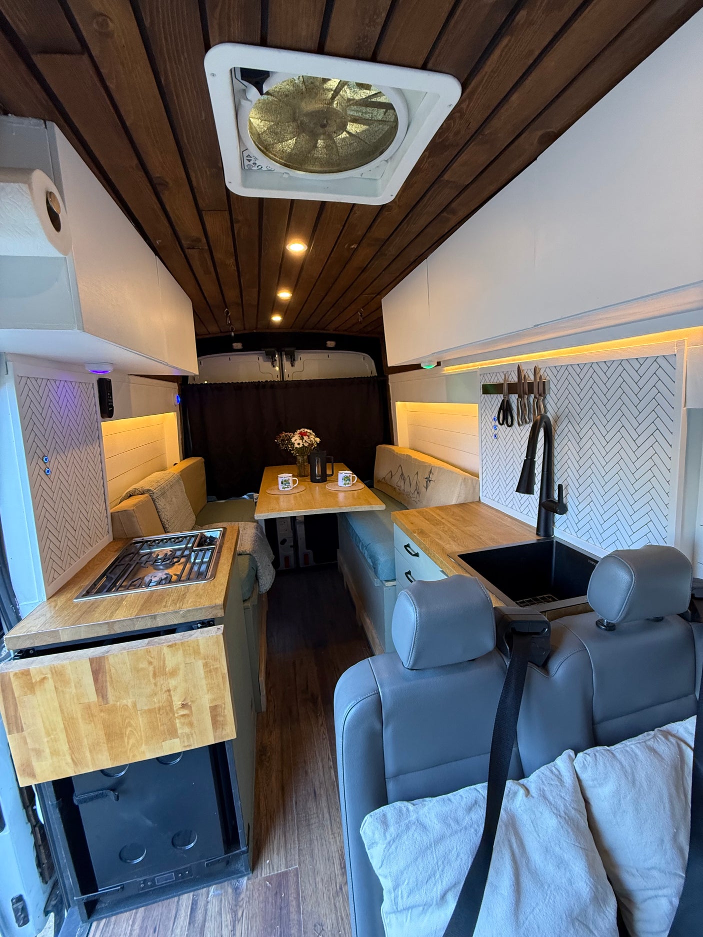 Spacious van conversion interior for rv rental with full kitchen, dining area, and cozy living space. Wood details & modern amenities.