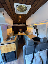 Spacious van conversion interior for rv rental with full kitchen, dining area, and cozy living space. Wood details & modern amenities.