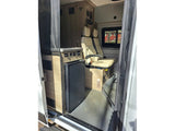 Inside an RV rental camper van: a compact kitchen with fridge, passenger seating, and a mesh screen door are visible from the entry.