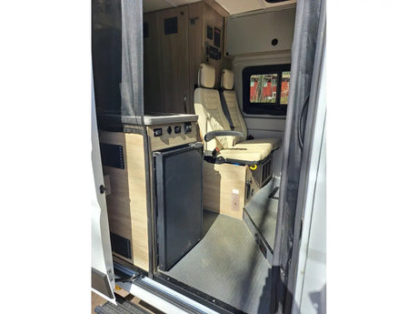 Inside an RV rental camper van: a compact kitchen with fridge, passenger seating, and a mesh screen door are visible from the entry.