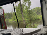 Enjoy a serene RV rental view from bed, featuring a screen window overlooking a tranquil lake and lush forest.