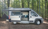 A modern rv rental camper van, with its interior open and awning extended, parked in a sunlit forest for outdoor camping.