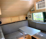 Bright rv rental interior featuring light wood paneling, a comfy grey dinette with table, and an AC unit.