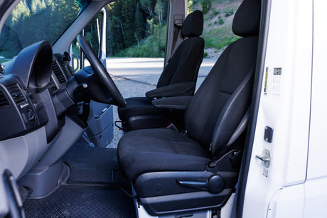 Interior of an RV rental van: driver and passenger seats, dashboard, and floor mats. Ready for your next adventure!