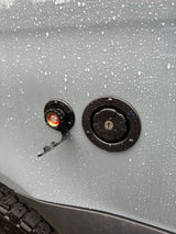 Rain-dusted RV rental exterior detailing water hookup points: a screened inlet and a locked fresh water fill.
