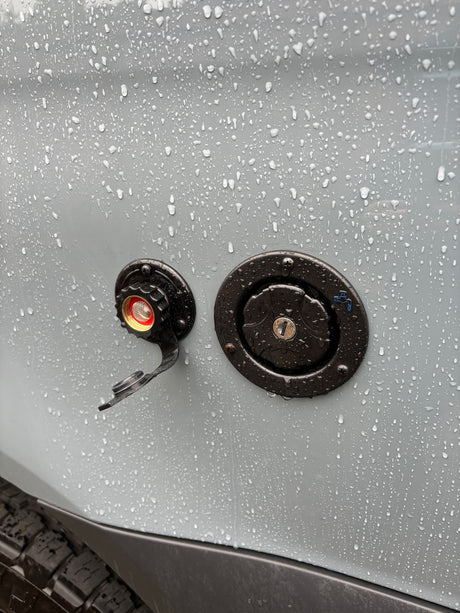 Rain-dusted RV rental exterior detailing water hookup points: a screened inlet and a locked fresh water fill.