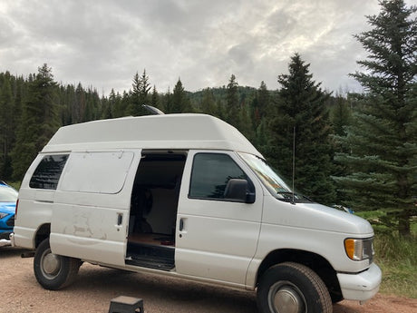 Spacious white high-top camper van, an ideal RV rental for exploring forests. Open door shows cozy interior for van life.