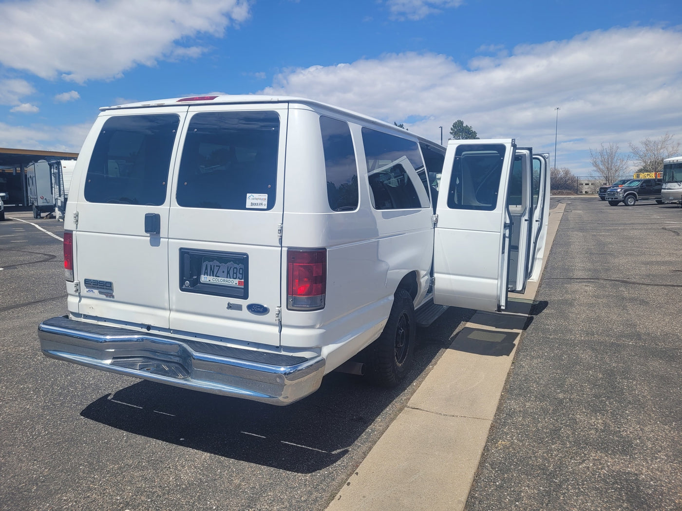 White Ford E-350 van, an ideal rv rental, is seen with its side doors open in a large parking lot alongside other RVs. — photo 6