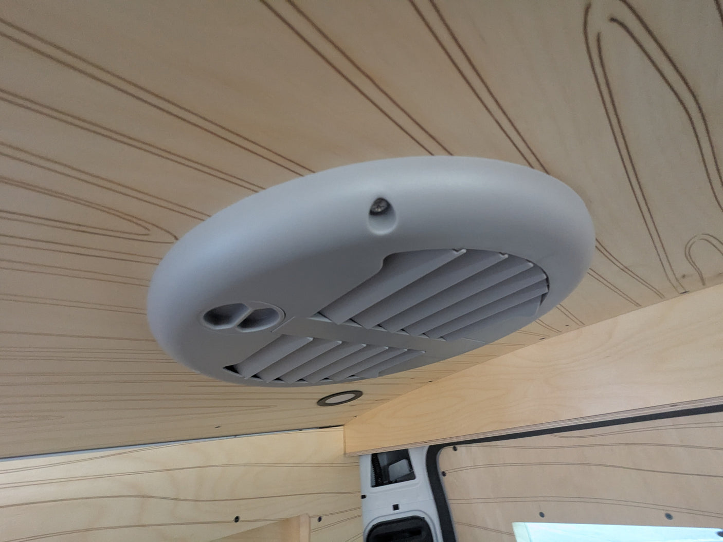 RV rental interior: View of the ceiling with a gray air vent/AC unit & light wood paneling featuring decorative grooves.