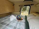 Cozy RV rental interior with a bed, S'mores kit, and an open hatch revealing an outdoor patio. Ready for adventures!