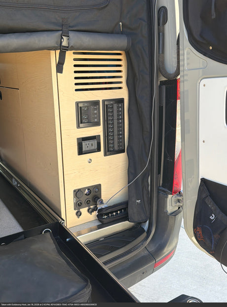 RV rental camper van interior, showcasing a power control panel with AC/USB outlets, a voltage meter, and integrated wooden storage.