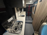 Compact rv rental campervan interior: featuring a well-equipped kitchen with stove and sink, comfortable bed, and storage solutions.