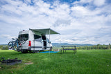 Enjoy an RV rental experience! White camper van with bikes in a grassy field, awning, picnic table & mountain views.