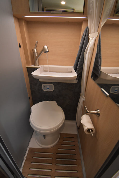 This RV rental's clever compact bathroom includes a toilet, sink, running water, shower curtain, and wood floor mat.