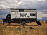 Rugged off-road camper, white with black hexagon trim, sits on rocky ground. Your next RV rental adventure awaits!