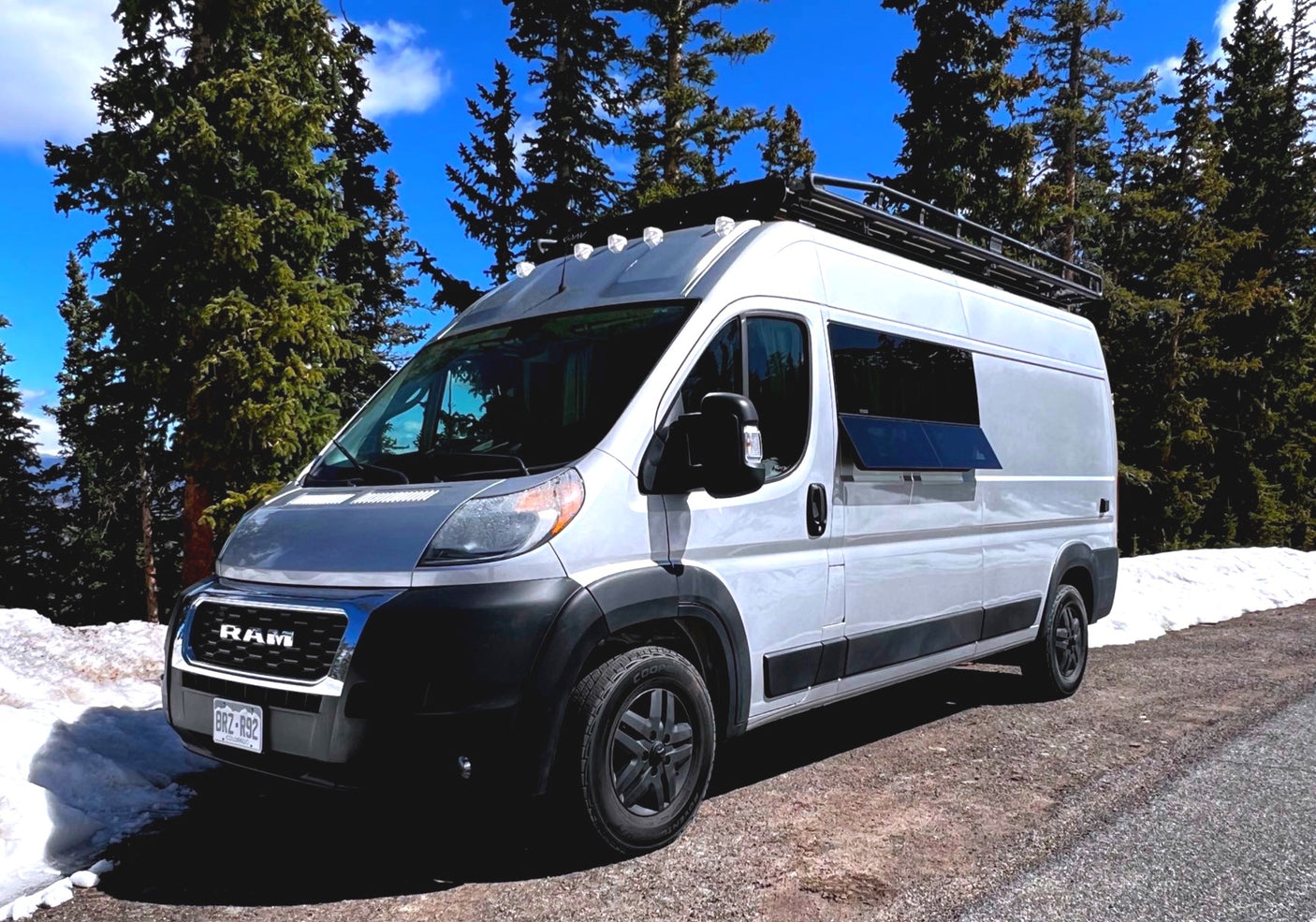 Exploring nature in a white RV rental camper van, parked on a snowy mountain road among tall pine trees.