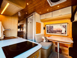Inside a stylish **rv rental**: bright kitchen with induction cooktop, cozy dining nook, and a compact shower/toilet.