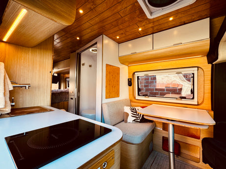 Inside a stylish **rv rental**: bright kitchen with induction cooktop, cozy dining nook, and a compact shower/toilet.