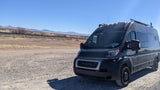 Adventure-ready dark gray Ram ProMaster camper van on a gravel road by railroad tracks & mountains. Perfect RV rental for off-grid travel.