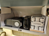 Compact kitchen setup in an **rv rental**, featuring a Keurig **coffee maker**, toaster, and a basket of **k-cups** with a "COFFEE" sign.
